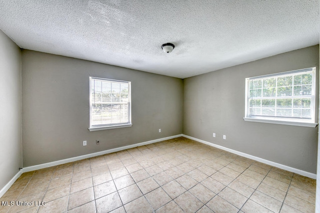 spare room with a textured ceiling, light tile patterned floors, and plenty of natural light