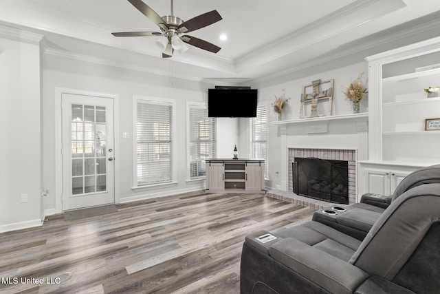 living room with ornamental molding, light wood-style floors, a fireplace, a raised ceiling, and ceiling fan