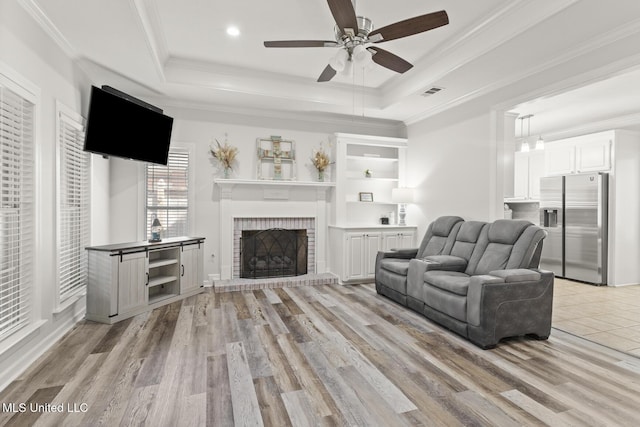 living room featuring light wood-style floors, a raised ceiling, crown molding, and visible vents