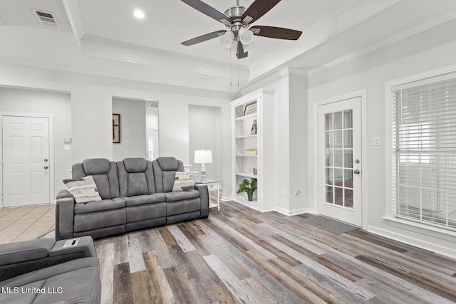 living room with built in shelves, wood finished floors, visible vents, crown molding, and a raised ceiling