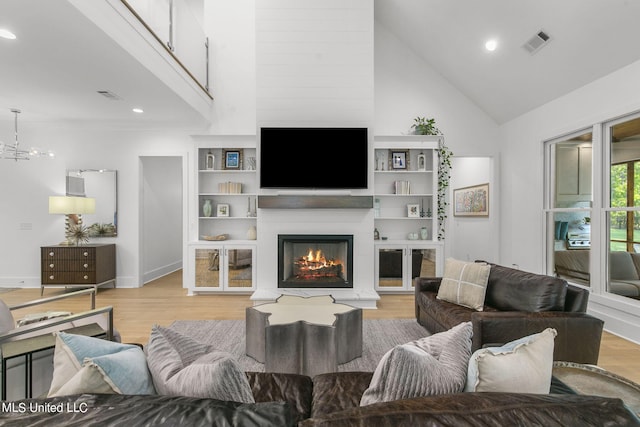 living room featuring built in features, a large fireplace, light hardwood / wood-style floors, and high vaulted ceiling