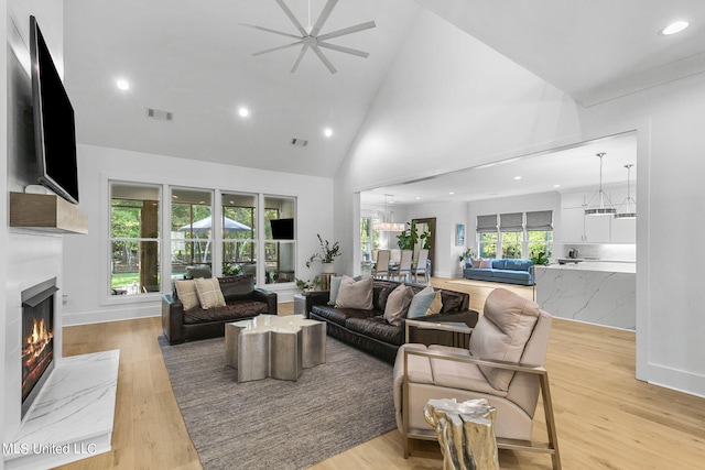 living room with light hardwood / wood-style floors, high vaulted ceiling, ceiling fan, and a healthy amount of sunlight