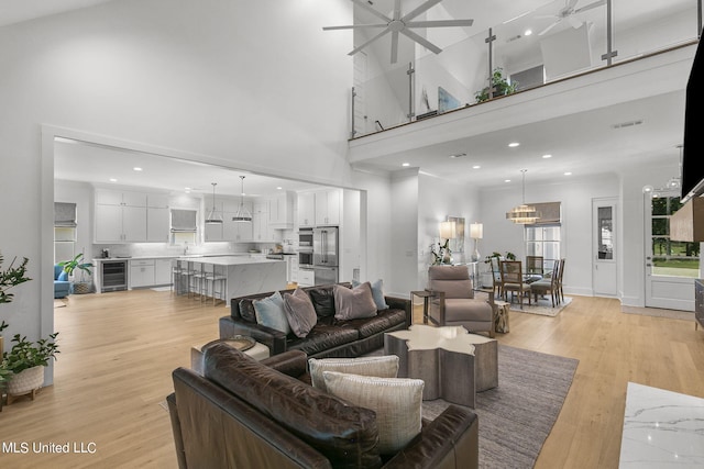 living room featuring a high ceiling, light wood-type flooring, wine cooler, and ceiling fan