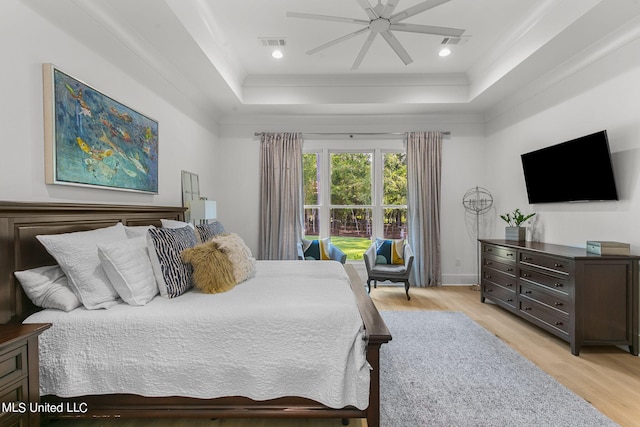 bedroom with light wood-type flooring, a tray ceiling, ceiling fan, and crown molding