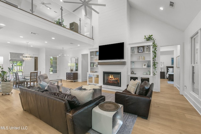 living room with a fireplace, a towering ceiling, ceiling fan with notable chandelier, and light hardwood / wood-style floors