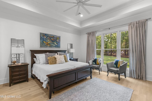 bedroom with ceiling fan, light hardwood / wood-style floors, and a tray ceiling