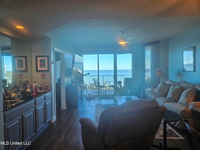 living room featuring a wealth of natural light, a water view, dark wood-type flooring, and ceiling fan