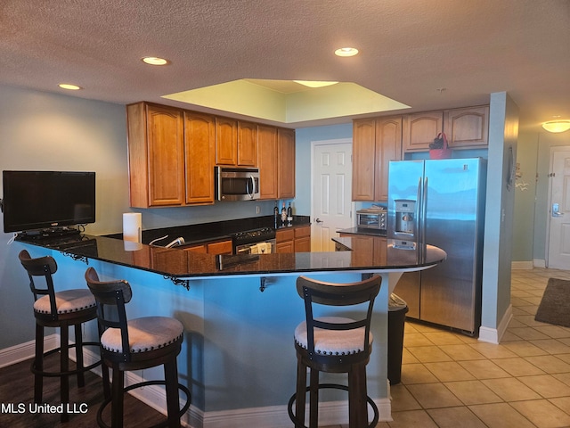 kitchen featuring a kitchen breakfast bar, kitchen peninsula, stainless steel appliances, and a textured ceiling