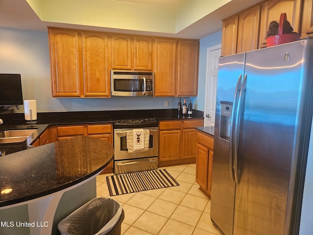 kitchen featuring dark stone counters, sink, light tile patterned floors, and stainless steel appliances