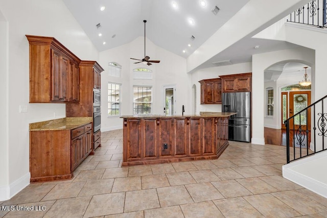 17000 River Pl, Vancleave, MS 39565 - kitchen featuring stainless steel appliances, ceiling fan, a large island with sink, arched walkways, and light stone counters