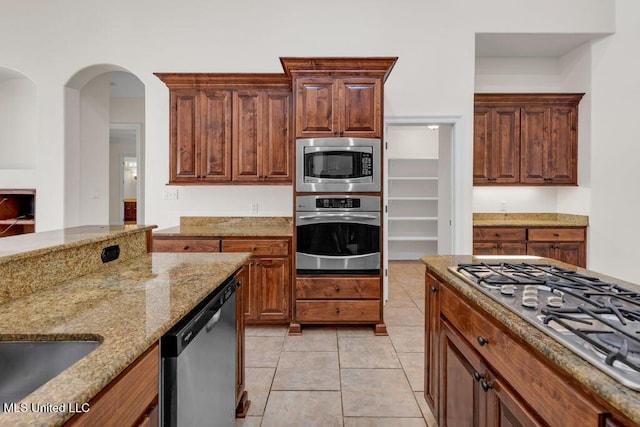 17000 River Pl, Vancleave, MS 39565 - kitchen featuring appliances with stainless steel finishes, light stone counters, light tile patterned flooring, a sink, and arched walkways