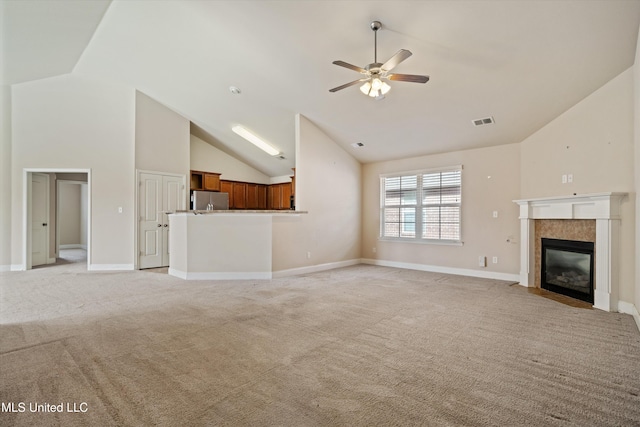 unfurnished living room with ceiling fan, light colored carpet, a tiled fireplace, and high vaulted ceiling