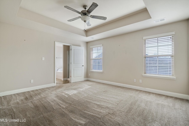 unfurnished bedroom with ensuite bathroom, a raised ceiling, and light carpet