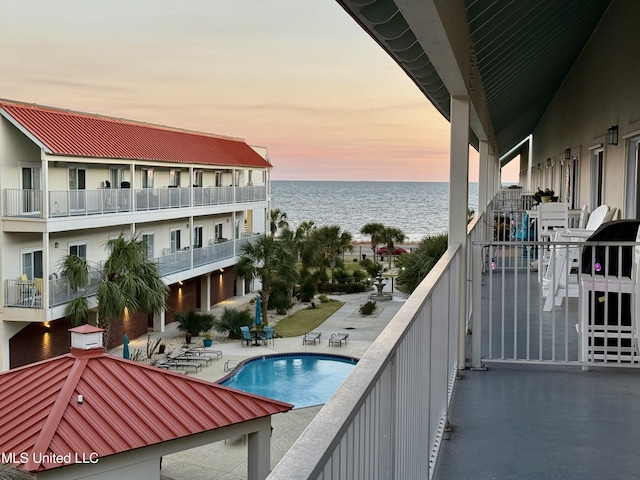 balcony at dusk featuring a patio and a water view