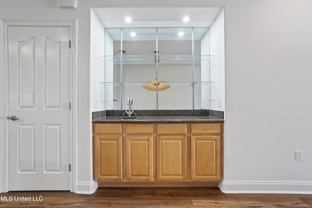 bar featuring dark wood finished floors, wet bar, baseboards, and a sink