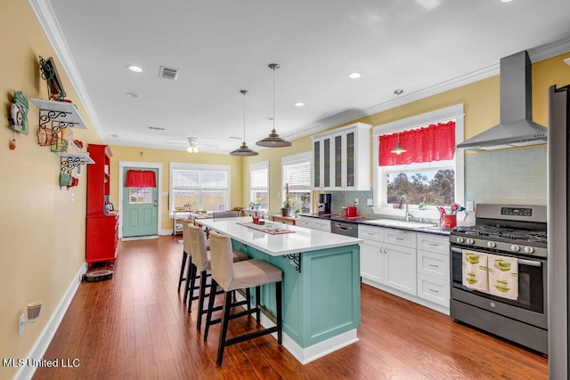 kitchen with visible vents, white cabinets, stainless steel range with gas stovetop, wall chimney range hood, and a sink