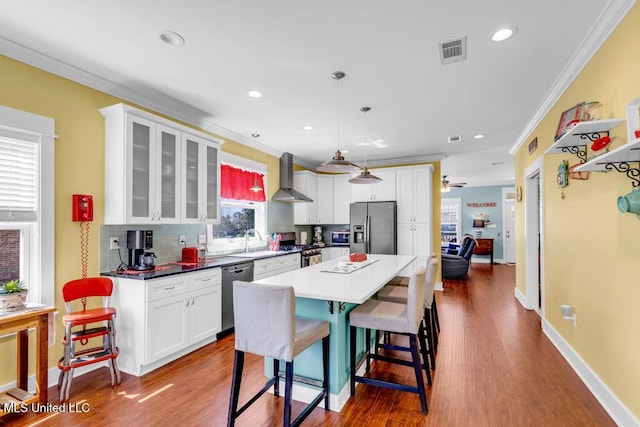 kitchen featuring crown molding, stainless steel appliances, visible vents, a sink, and wall chimney range hood