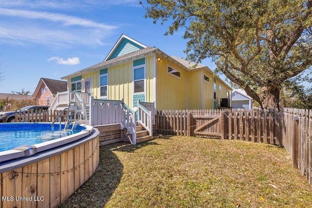 back of house featuring a fenced backyard, a lawn, a fenced in pool, and a wooden deck