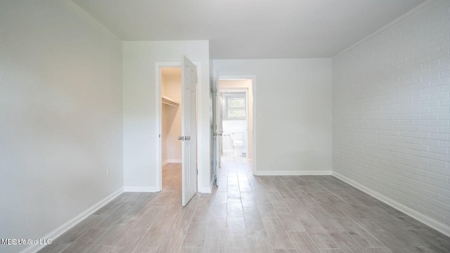 unfurnished bedroom with baseboards, brick wall, and wood finished floors