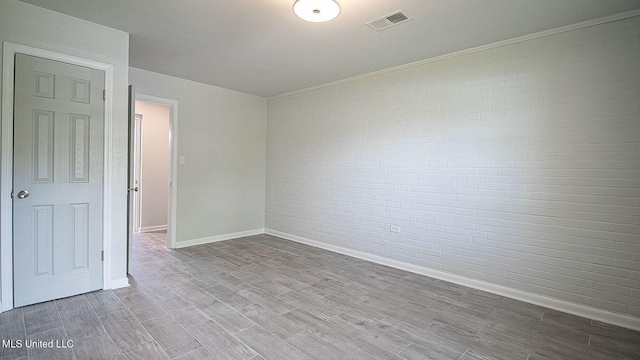 unfurnished room with brick wall, wood finished floors, visible vents, and baseboards