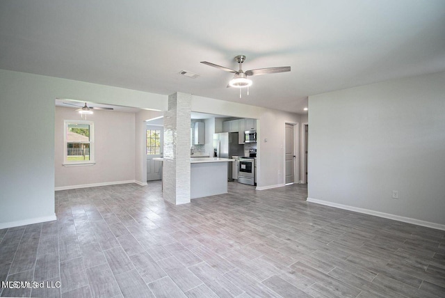 unfurnished living room featuring baseboards, visible vents, a ceiling fan, and wood finished floors