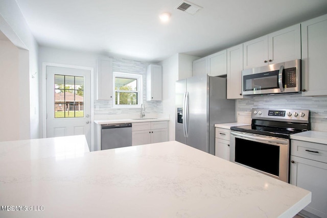 kitchen with a sink, visible vents, appliances with stainless steel finishes, backsplash, and light stone countertops