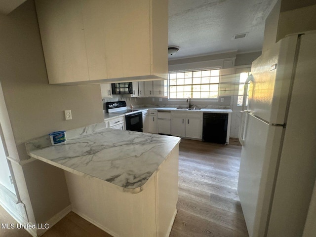 kitchen with light wood finished floors, a peninsula, white cabinets, black appliances, and a sink