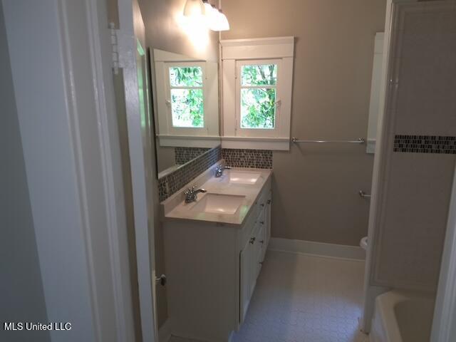 3 New St, Natchez, MS 39120 - full bathroom with double vanity, baseboards, toilet, a bath, and backsplash