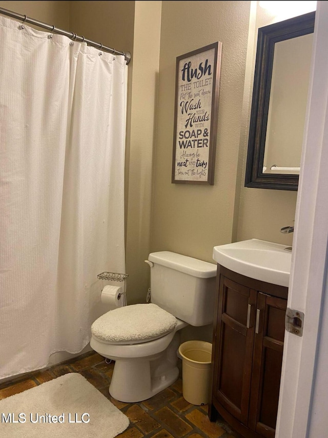 full bath with a shower with curtain, toilet, vanity, and brick floor