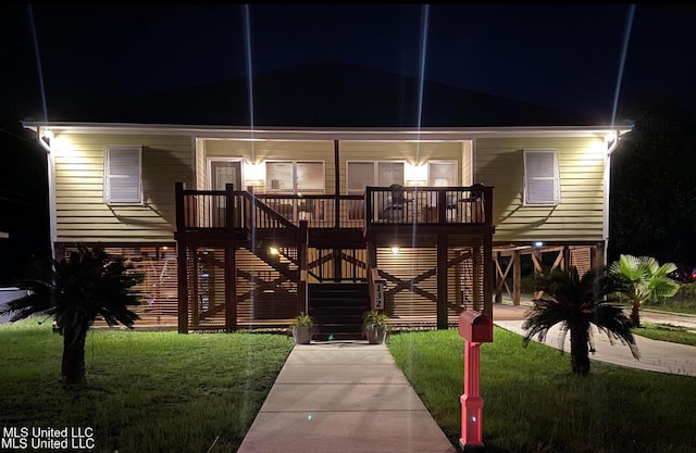 back of house at night featuring a lawn, a porch, and stairway
