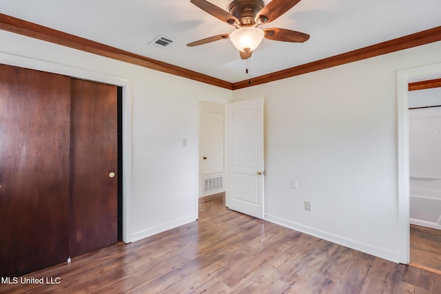 unfurnished bedroom featuring crown molding, a closet, visible vents, and wood finished floors