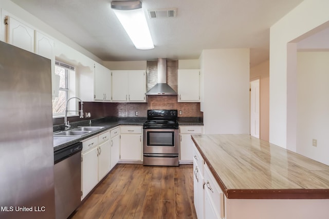 kitchen with a sink, visible vents, wall chimney exhaust hood, white cabinetry, and appliances with stainless steel finishes