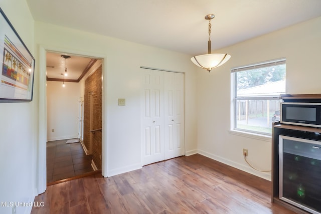 kitchen featuring wood finished floors, wine cooler, decorative light fixtures, ornamental molding, and baseboards