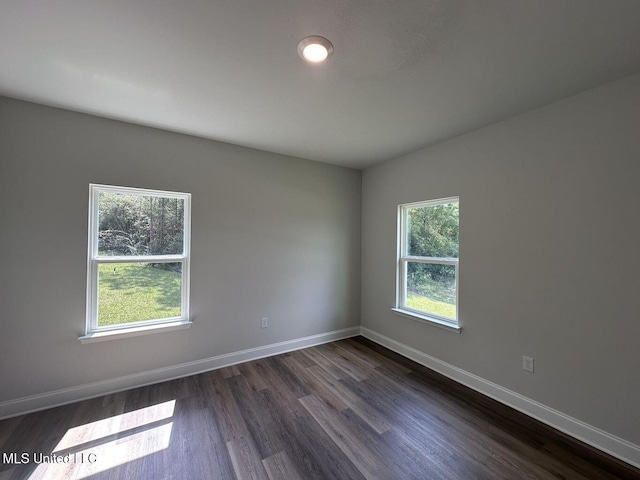 empty room with dark wood-style floors, a healthy amount of sunlight, and baseboards