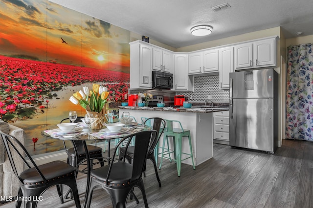 kitchen featuring white cabinets, dark stone countertops, stainless steel appliances, and dark hardwood / wood-style flooring