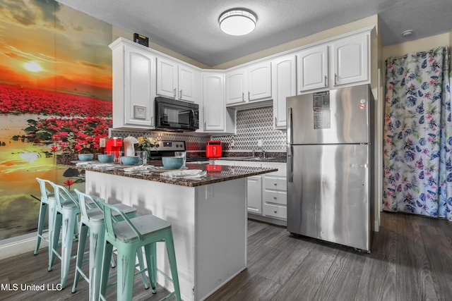 kitchen featuring tasteful backsplash, appliances with stainless steel finishes, white cabinetry, dark wood-type flooring, and a breakfast bar