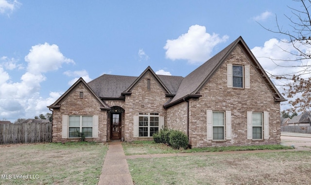 view of front of property featuring a shingled roof, fence, a front lawn, and brick siding