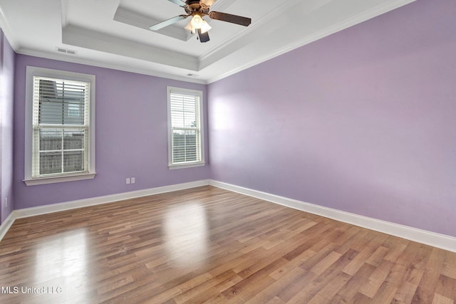 empty room with visible vents, a raised ceiling, crown molding, and wood finished floors