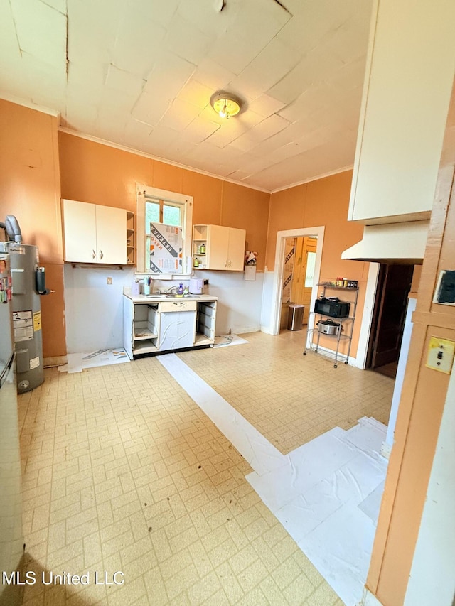 1057 Adams St, Grenada, MS 38901 - kitchen with electric water heater, light flooring, crown molding, open shelves, and white cabinetry