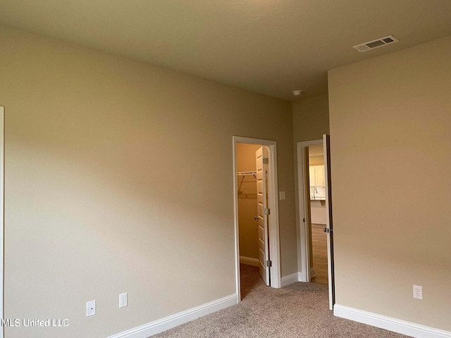 unfurnished bedroom with a closet, light colored carpet, and a walk in closet