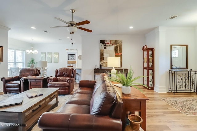 living room with ceiling fan with notable chandelier, ornamental molding, and light hardwood / wood-style floors