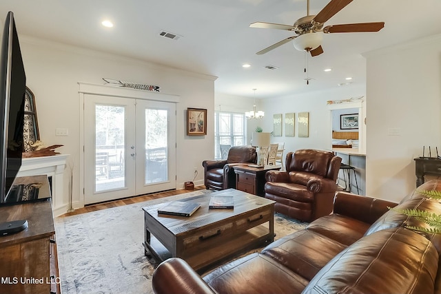 living room with crown molding, ceiling fan with notable chandelier, light wood-type flooring, and french doors