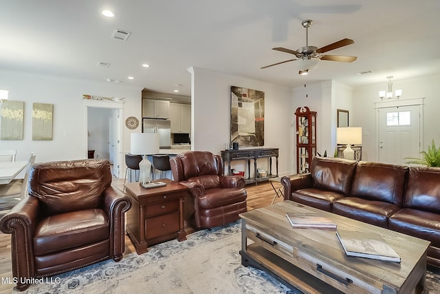 living room with ceiling fan with notable chandelier and light hardwood / wood-style floors