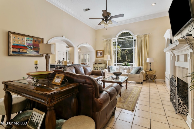 living room featuring a high ceiling, a tiled fireplace, ornamental molding, light tile patterned floors, and ceiling fan