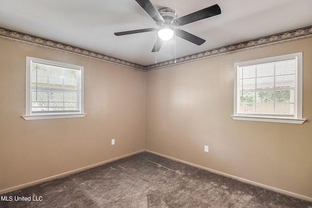 empty room with a wealth of natural light, dark carpet, and ceiling fan