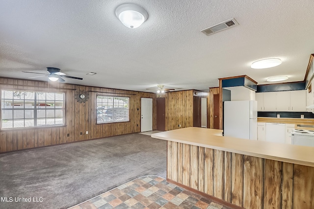 kitchen with wood walls, carpet floors, white cabinets, and white appliances