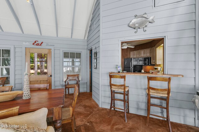 dining room featuring wooden walls, vaulted ceiling, and ceiling fan