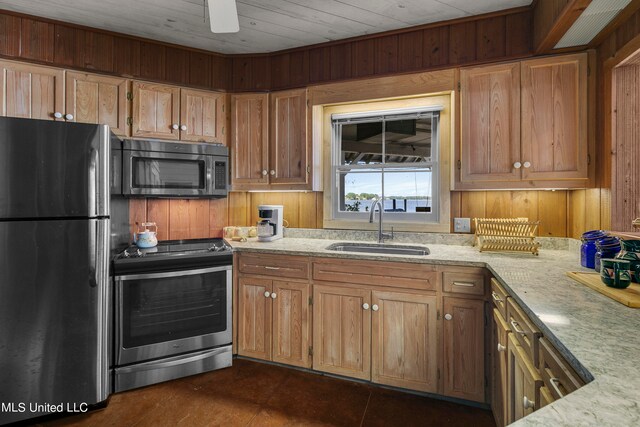 kitchen featuring sink, light stone counters, stainless steel appliances, and wood walls