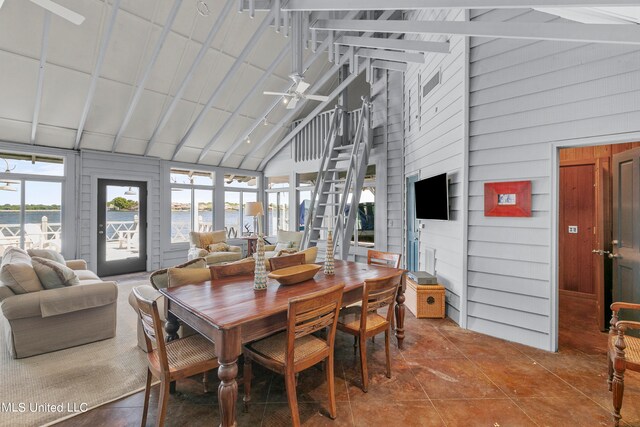 tiled dining space with ceiling fan, wood walls, and high vaulted ceiling