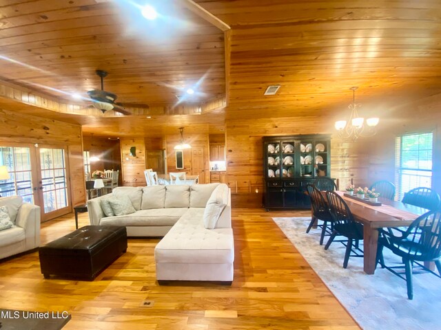 living room with wood ceiling, wood walls, ceiling fan with notable chandelier, light hardwood / wood-style floors, and french doors